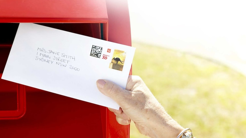 A woman places a letter in an Australia Post box.