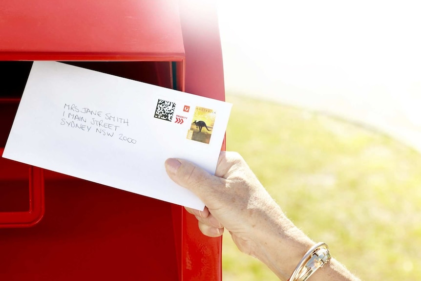 A woman places a letter in an Australia Post box.