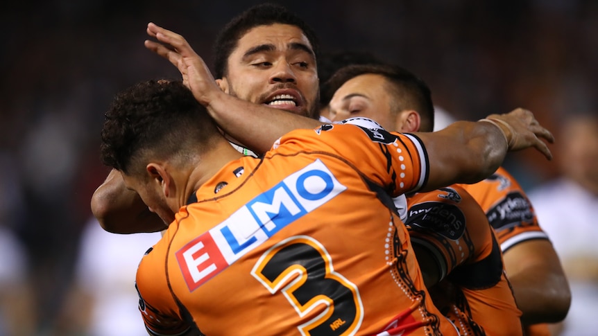 A Parramatta Eels NRL player is tackled by two Wests Tigers opponents.