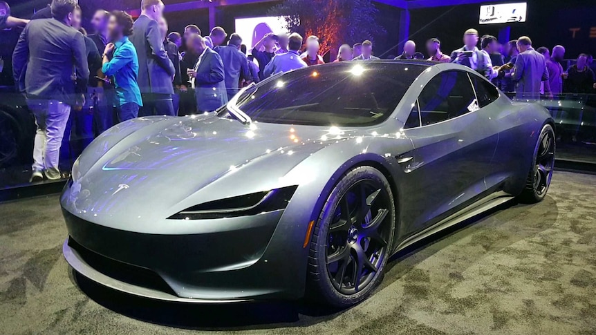 suited people surround an exhibited sports car