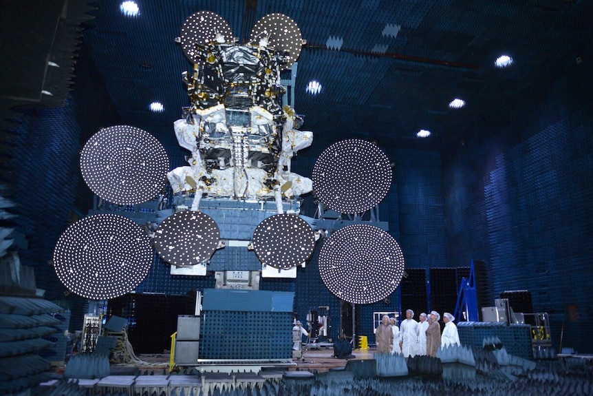 A group of people look at a satellite as it's being built.