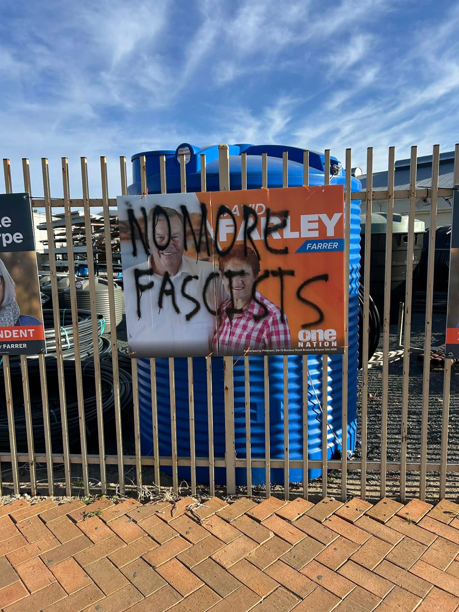 An orange One Nation poster with graffiti reading No more facists scrawled over it attached to a fence
