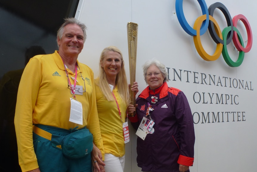 Laurie and Barabara smith wearing Team Australia tracksuits while holding the Olympic flame. 