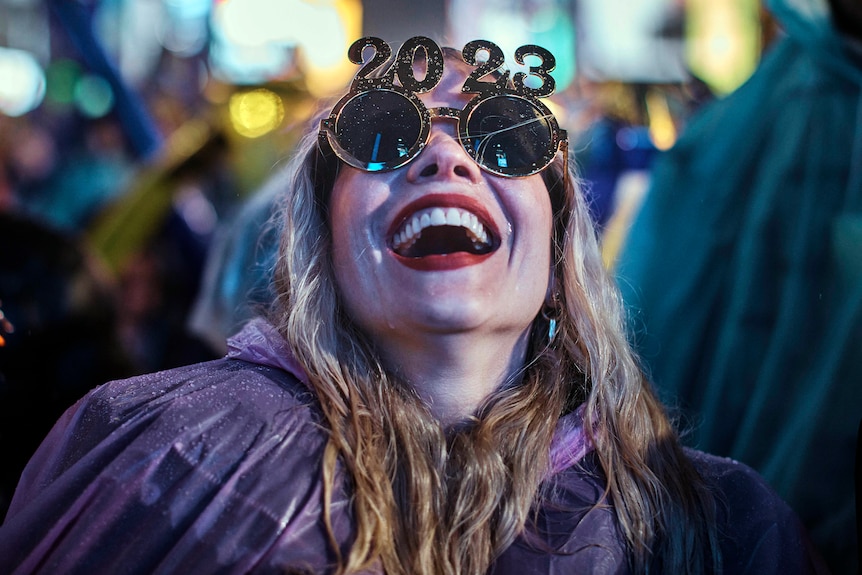 A reveller wearing 2023 sunglasses laughs as she waits for the countdown during New Year's Eve celebrations.