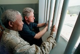 Nelson Mandela and Bill Clinton stand next to each other holding prison bars looking outside a prison window together