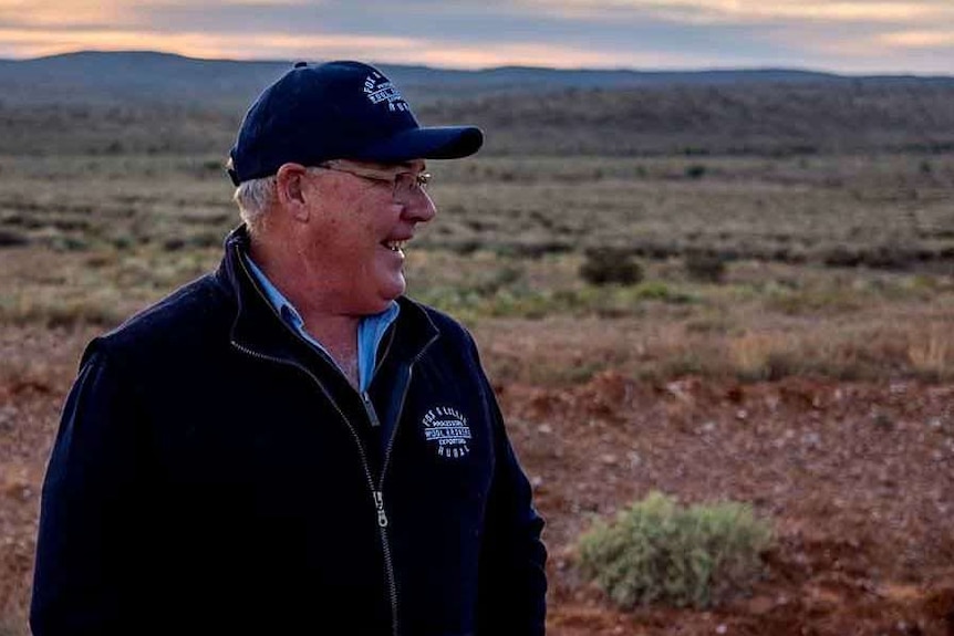 man stands in open paddock smiling