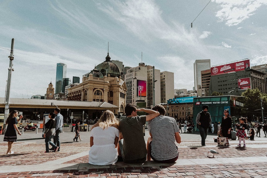 Three young friends sit together in Melbourne's Fed Square to depict how to make and keep friends after leaving high school.