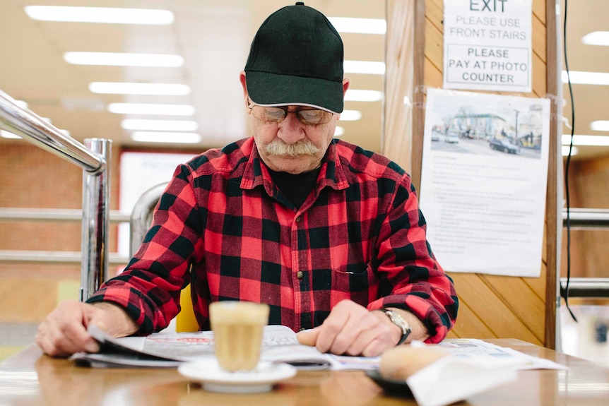 Older man Gitino reads the paper with a coffee