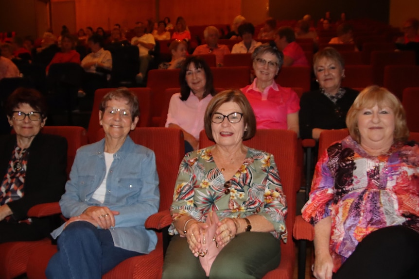 a group of women with multicolored shirts sitting in a cinema theatre smiling
