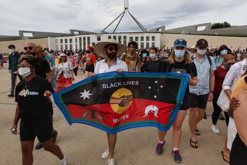 Protesters hold a sign saying "black lives matter" outside Australia's Parliament House in Canberra on Australia Day
