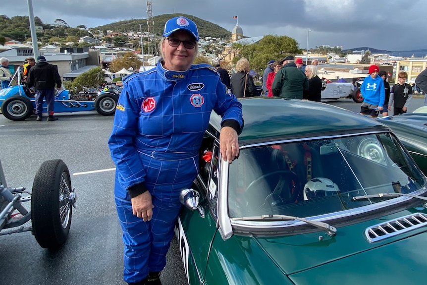 Sarah Fry stands beside her green race car wearing blue protective jumsuit