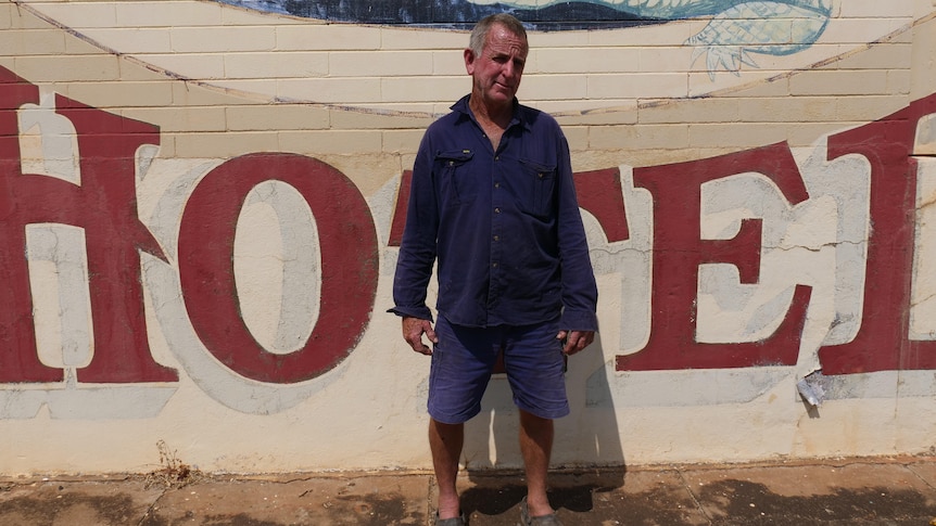 A man stands in front of a brick wall with 'hotel' and a croc painted on it.