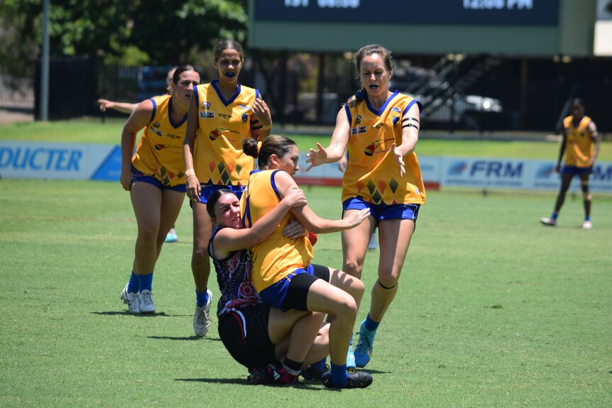 A Wanderers player is tackled as teammates run to support her.