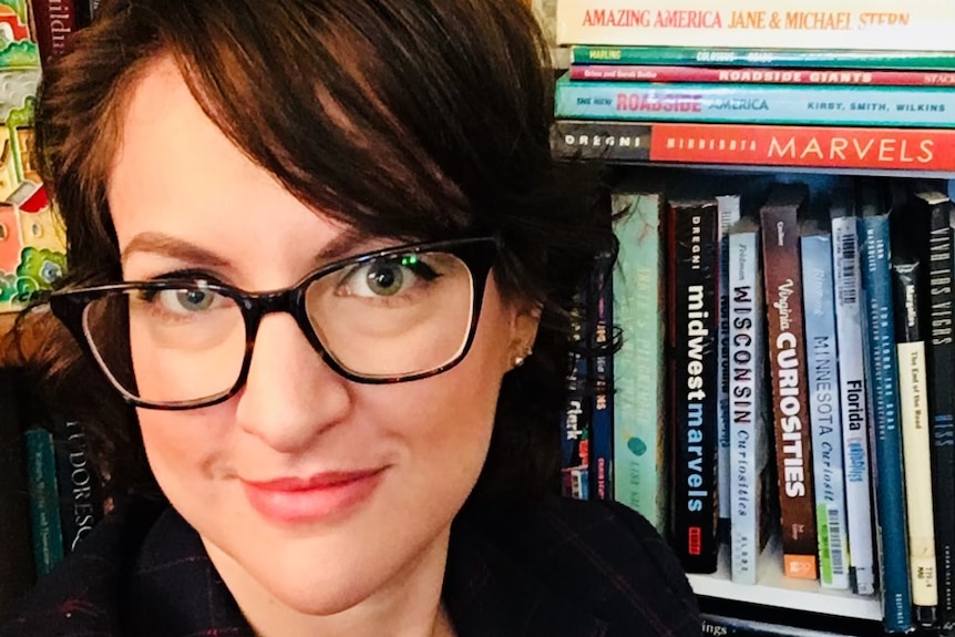 A portrait of a woman with glasses on in front of a bookshelve
