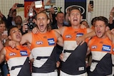 AFL players stand in a huddle in the dressing room singing their team song after victory