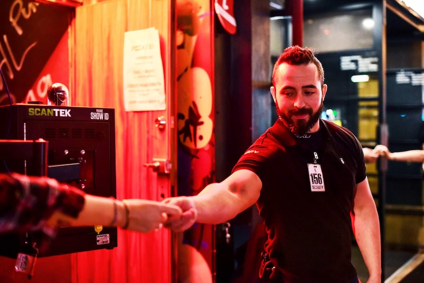 A bouncer standing next to an ID scanner takes ID off patron.