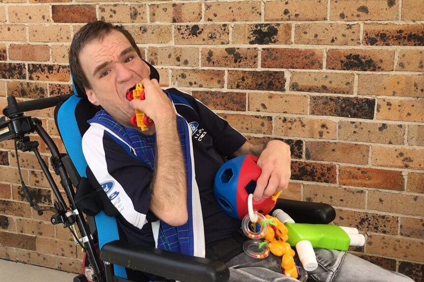 Colin Burchell plays with toys in his mobility chair.