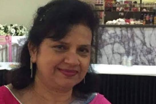 A woman wearing a pink sari smiles at the camera.