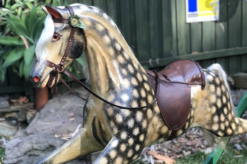 A large wooden rocking horse with a spotted body and green stand