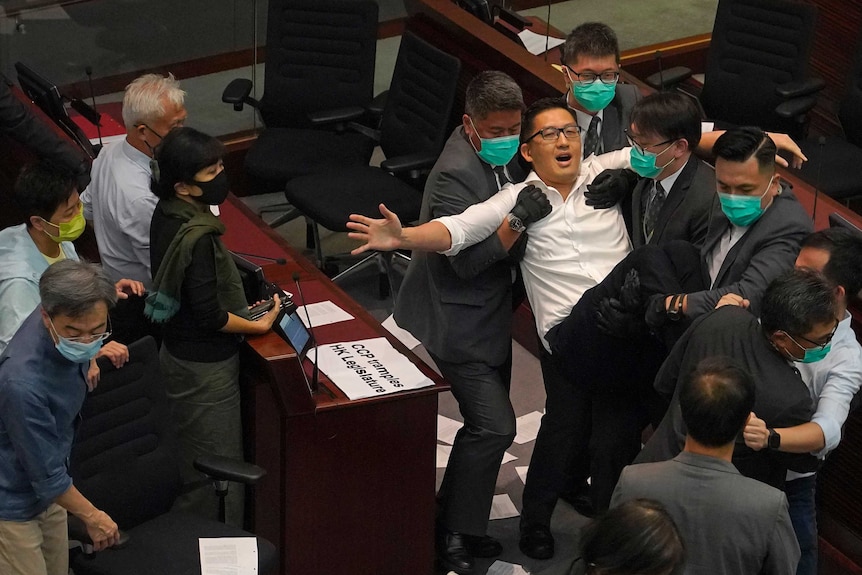 A man is held by a group of mask-wearing guards and carried out.