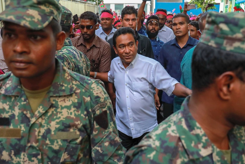 Maldivian President Abdulla Yameen walks along surrounded by body guards and other people.