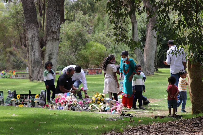 Aishwarya Aswath's father kneeling down and laying flowers, surrounded by people