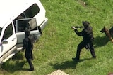 Three armed tactical police with a dog search a white four wheel drive with their guns drawn.