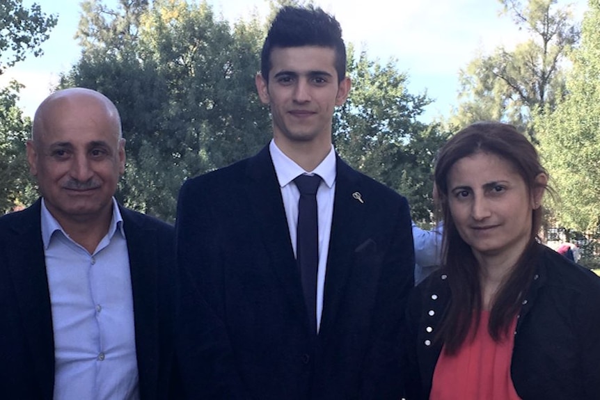 A man, his son and his wife in front of green trees and blue sky.