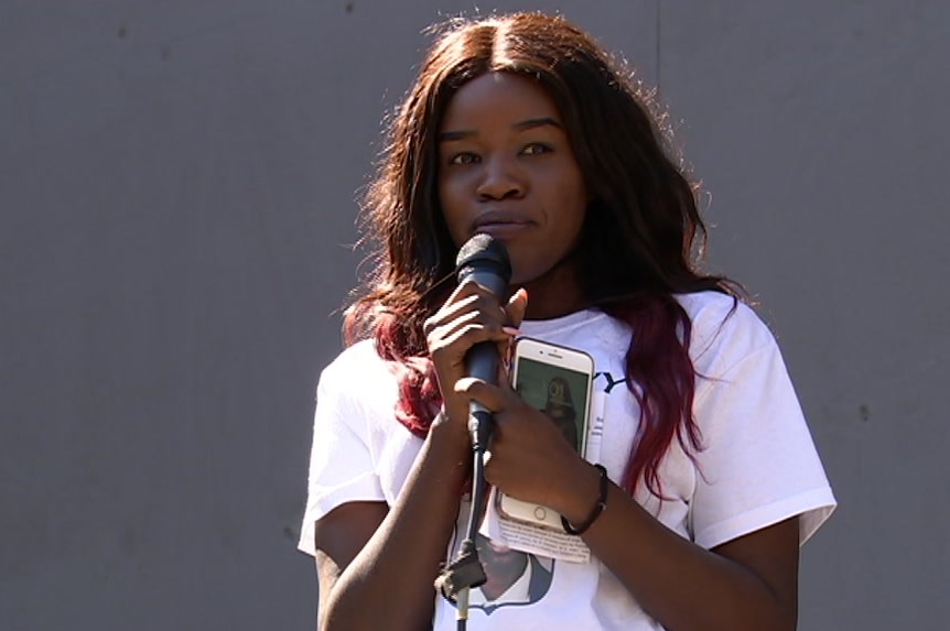 Nyawech Fouche holds a microphone and stands as she delivers her speech at the memorial.