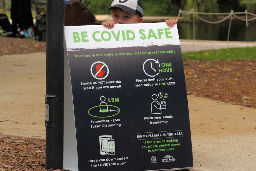 A boy holds on to a Be COVID safe sign at a park