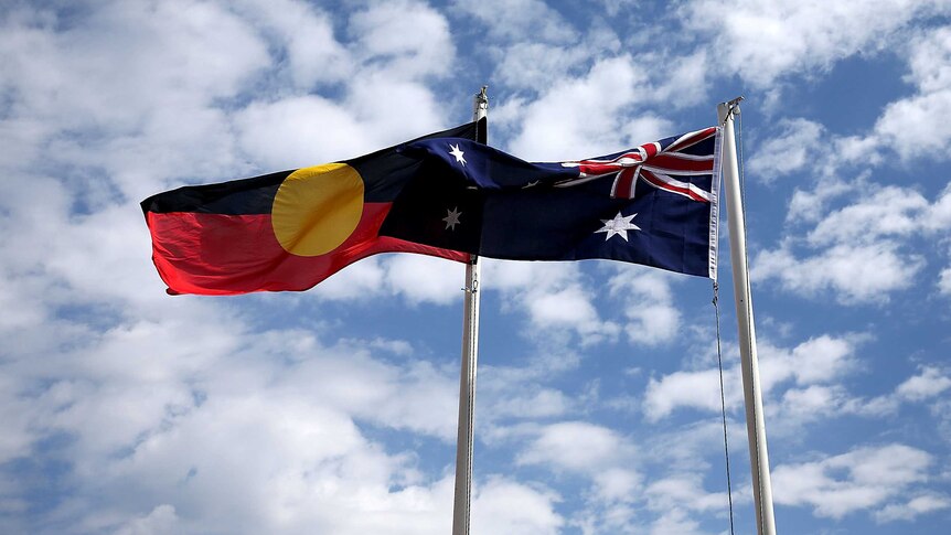 The Aboriginal flag and Australian flag fly side by side against a blue cloudy sky