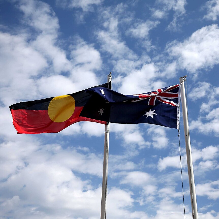 The Aboriginal flag and Australian flag fly side by side against a blue cloudy sky