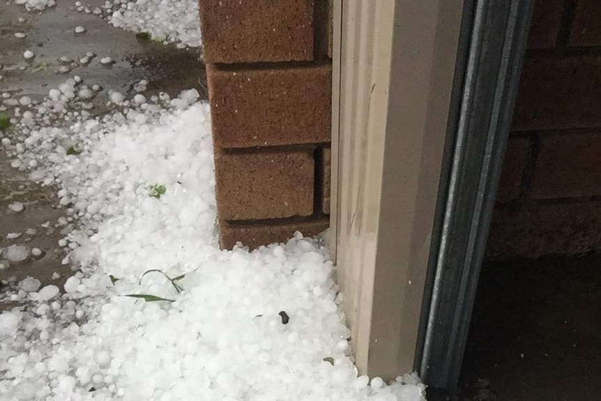 A close up of a pile of hail surrounding a brick home.