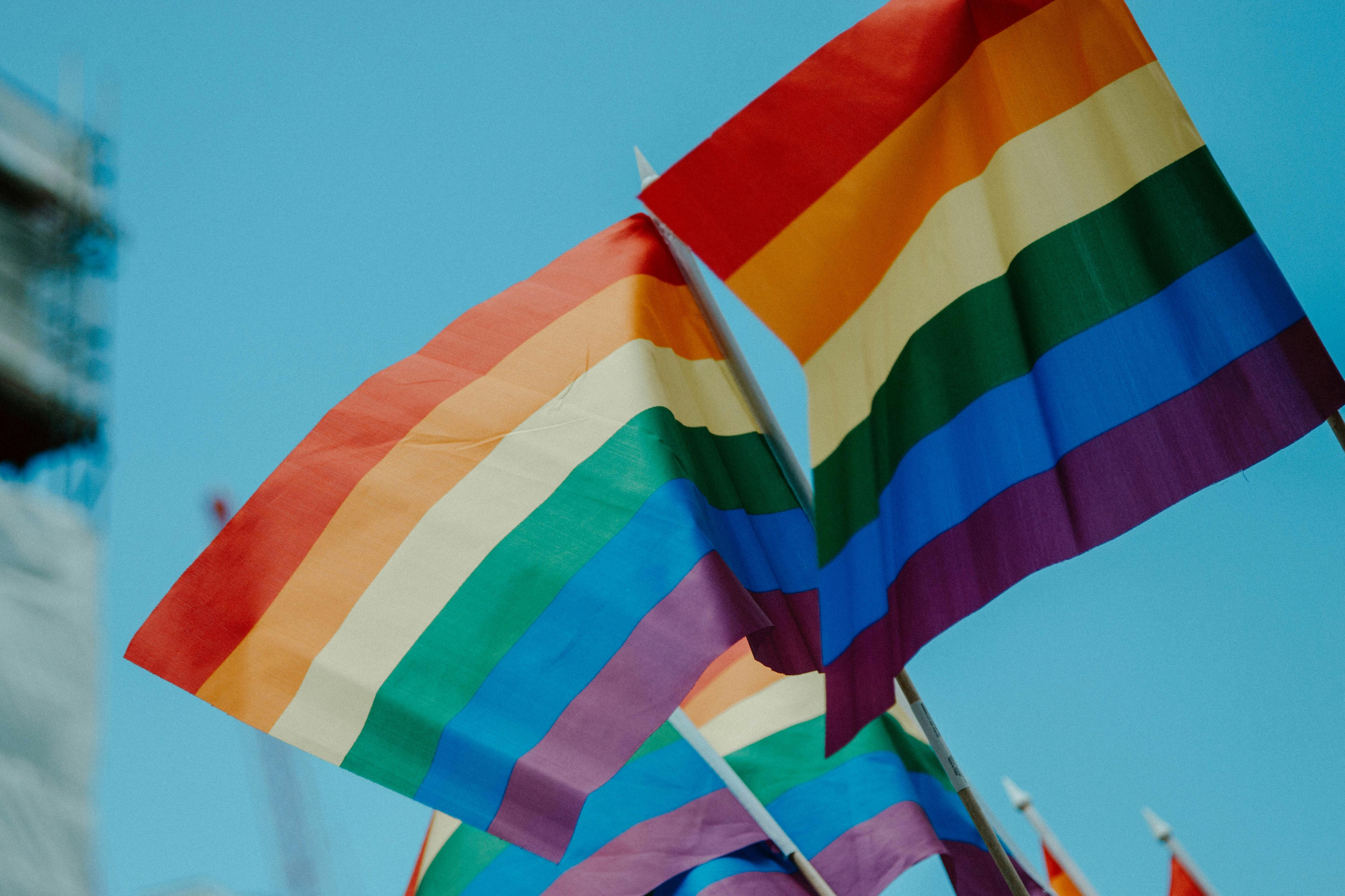 two rainbow flags against a blue sky