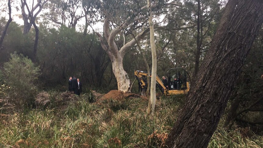 An excavator and police search bushland.