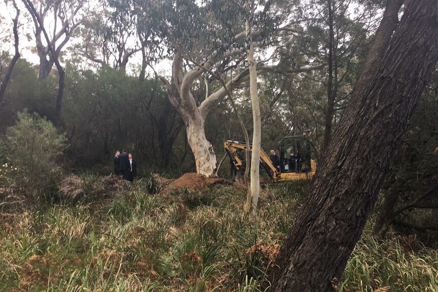 An excavator and police search bushland.