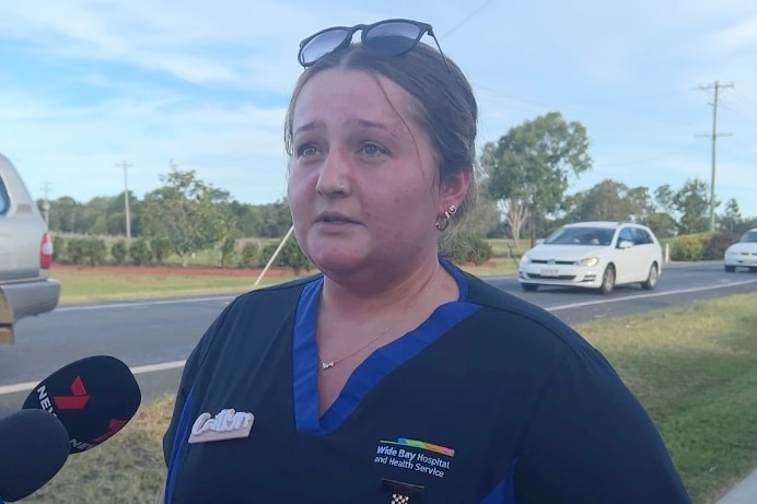 A woman in a nurses uniform places speaking to reporters, who's microphones can be seen in shot.