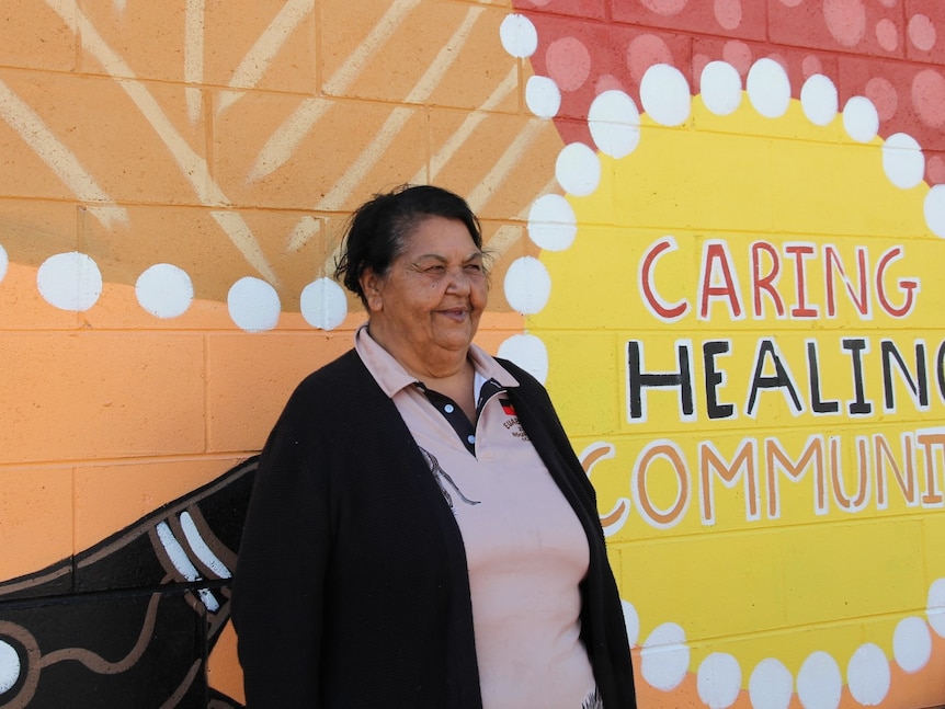 a woman standing in front of a colourful mural with words caring, healing , community written.