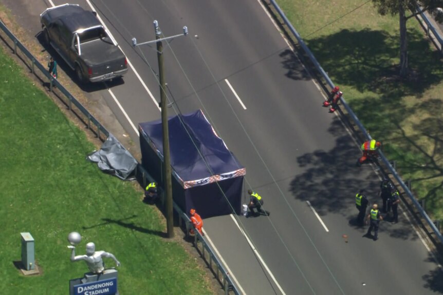 A blue tent set up on the side of the road with emergency services walking on the road and a car parked