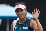 Peng Shuai waves while wearing tennis gear and visor
