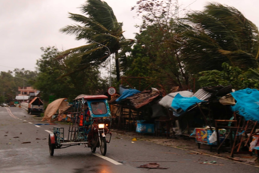 A man drives his tricycle along a road as strong winds caused by typhoon Vongfong