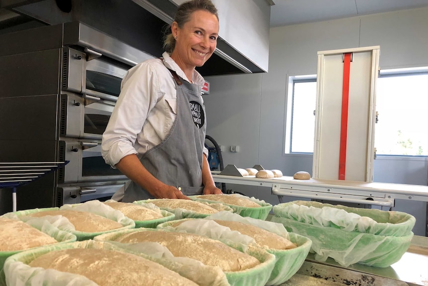 A baker smiling in front of the oven as she puts in the dough she has prepared