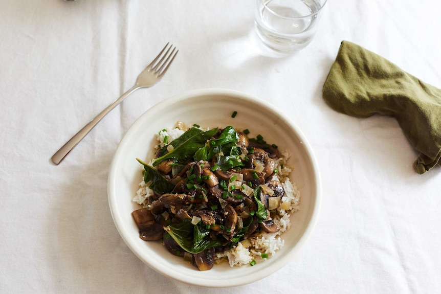 A bowl of mushroom stroganoff with baby spinach and chives served over rice, a warming and hearty vegetarian dinner recipe.