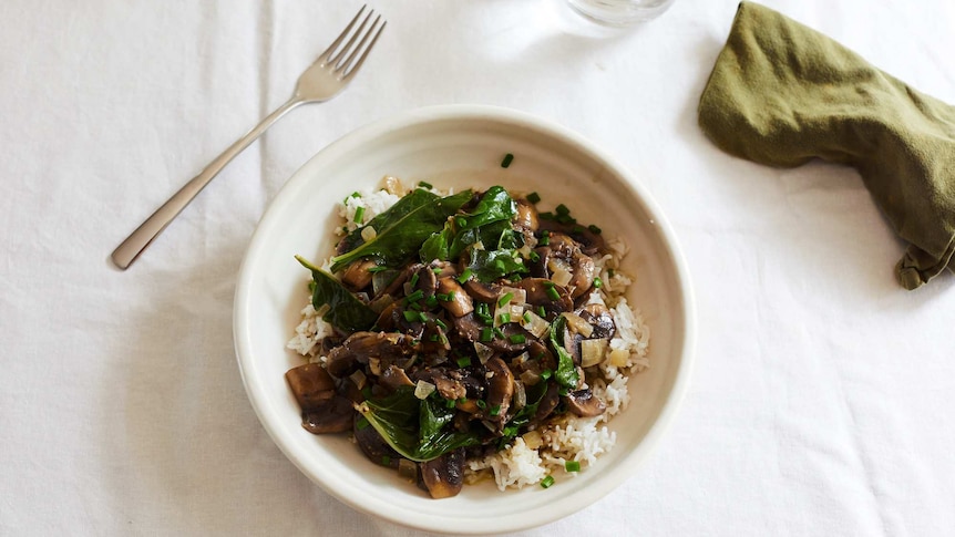 A bowl of mushroom stroganoff with baby spinach and chives served over rice, a warming and hearty vegetarian dinner for the winter.