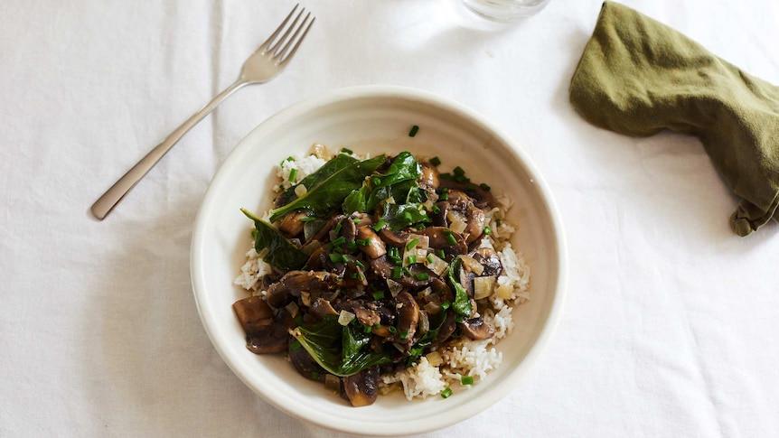 A bowl of mushroom stroganoff with baby spinach and chives served over rice, a warming and hearty vegetarian dinner recipe.