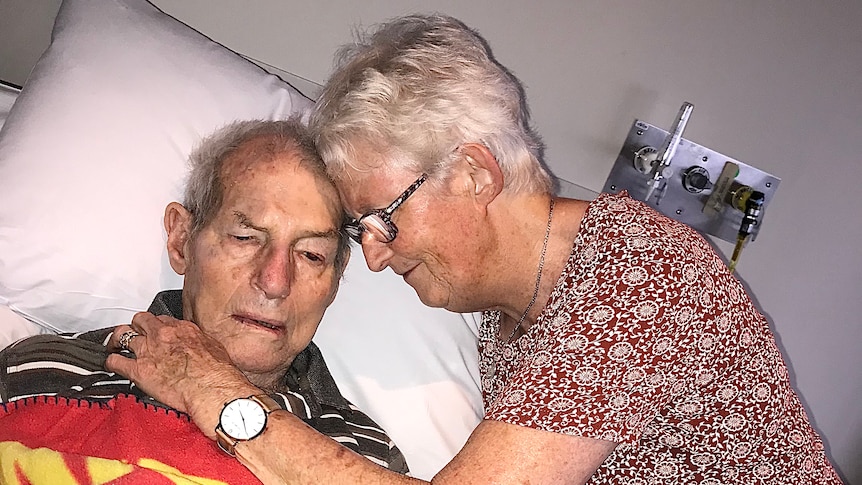 A woman leans down to hug a man in a hospital bed