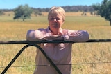 A woman leaning against a paddock fence.