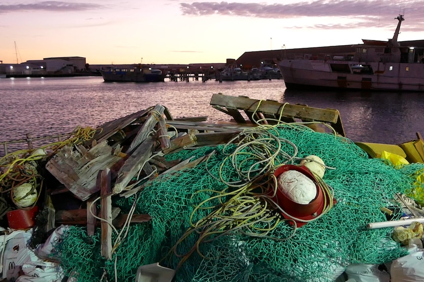 pile of net and floats, wood and rope on the back of a fishing boat at dawn with boats in background