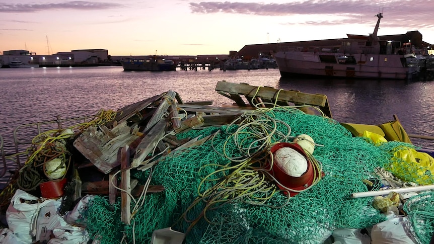 pile of net and floats, wood and rope on the back of a fishing boat at dawn with boats in background