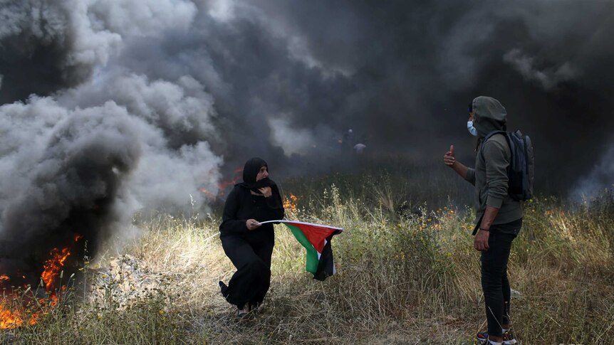 A woman is seen holding a Palestinian flag and surrounded by heavy smoke, while a young man gestures to her to move away.